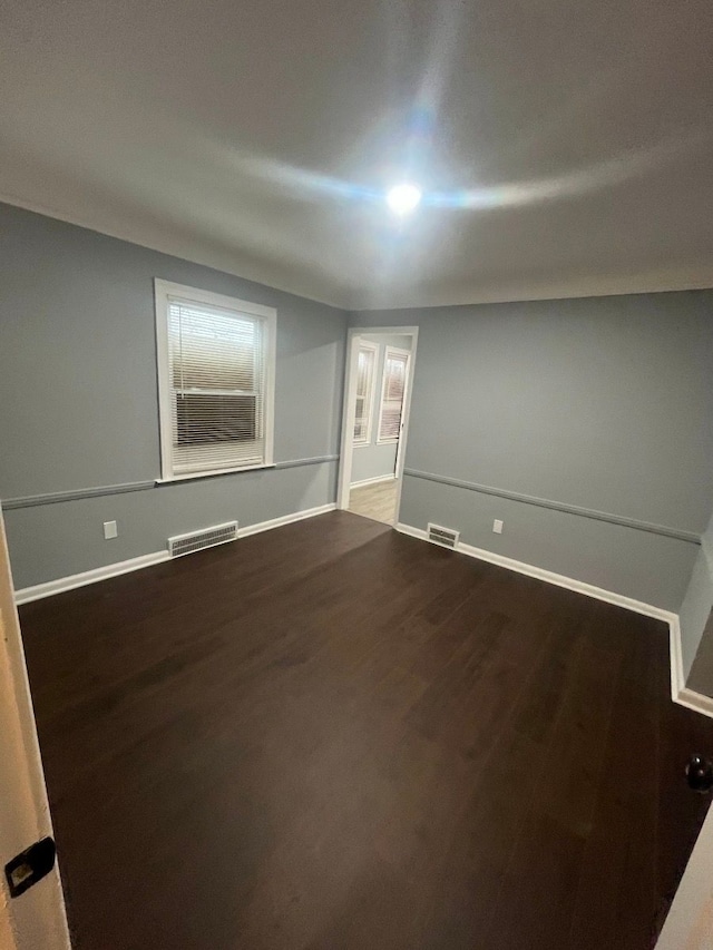 spare room with visible vents, baseboards, and dark wood-type flooring