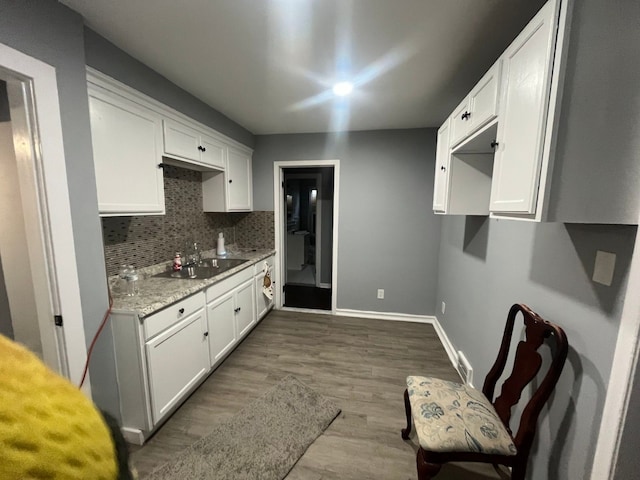 kitchen featuring dark wood-type flooring, a sink, backsplash, white cabinetry, and baseboards