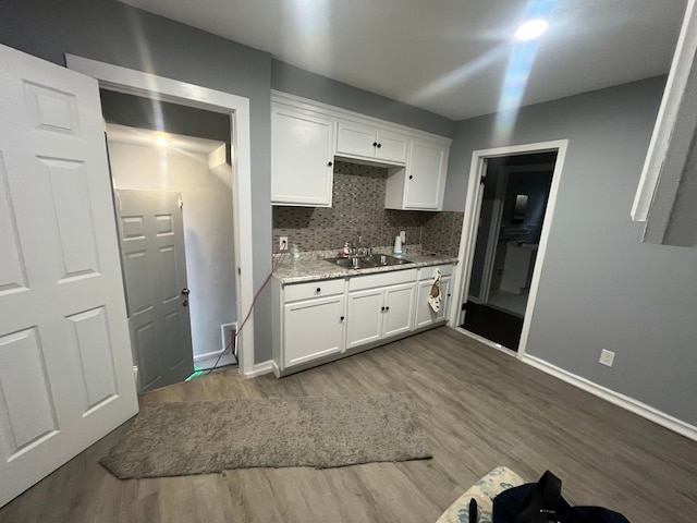 kitchen featuring tasteful backsplash, baseboards, wood finished floors, white cabinets, and a sink