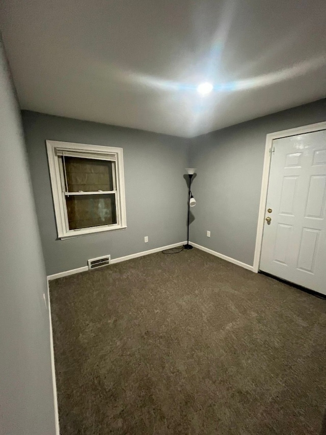 empty room with baseboards, visible vents, and dark carpet