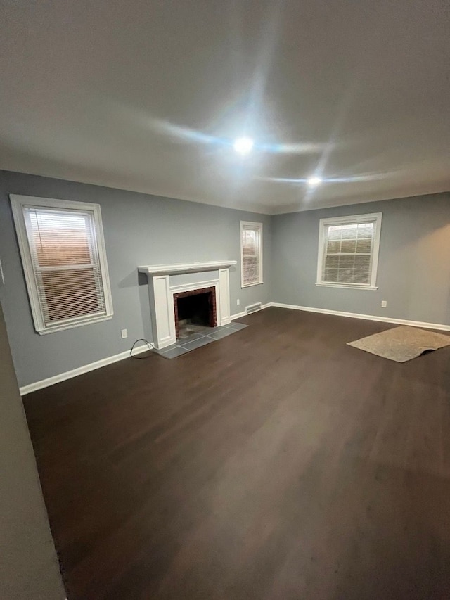 unfurnished living room with dark wood-type flooring, a fireplace with flush hearth, visible vents, and baseboards