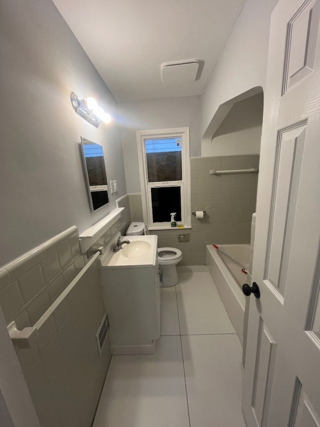 bathroom with tile patterned floors, visible vents, toilet, tile walls, and wainscoting