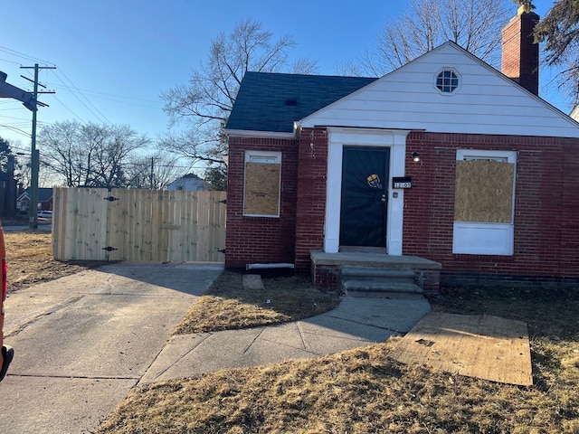 bungalow-style home with brick siding, roof with shingles, and fence