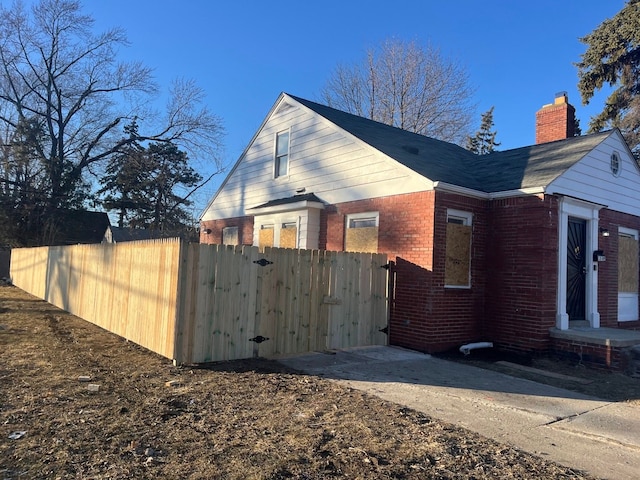 view of side of home with a gate, brick siding, a chimney, and fence