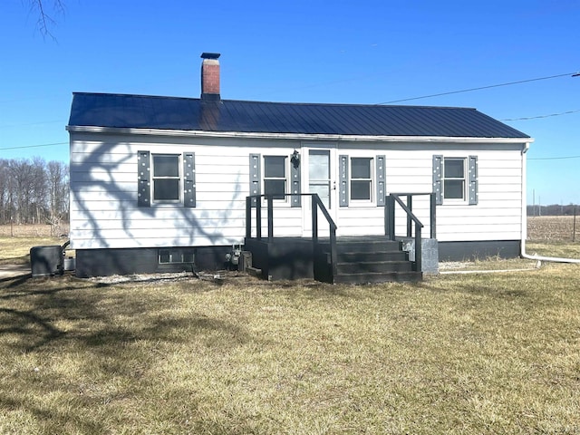 view of front of property featuring metal roof, a chimney, and a front lawn