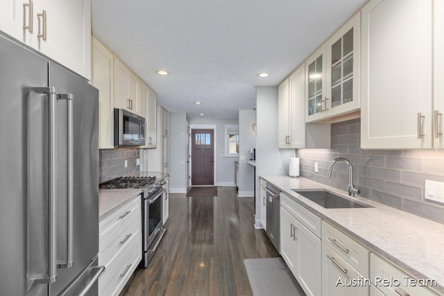 kitchen featuring dark wood-type flooring, a sink, glass insert cabinets, baseboards, and high end appliances