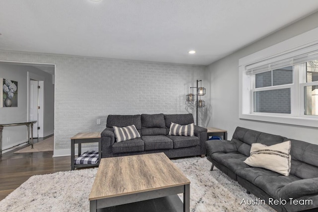 living area with recessed lighting, wood finished floors, baseboards, and brick wall
