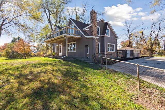 view of front facade with a front lawn, fence, a chimney, a balcony, and stone siding