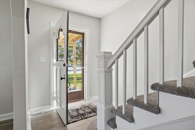 foyer entrance featuring stairway, baseboards, a textured ceiling, and wood finished floors