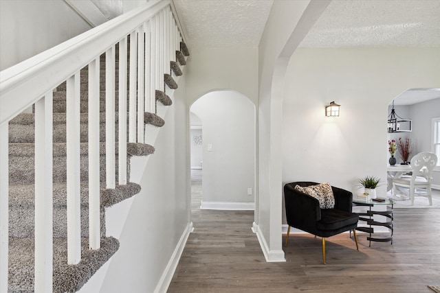hall featuring baseboards, arched walkways, a textured ceiling, and wood finished floors