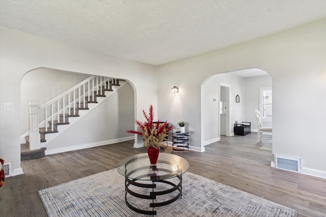 living area with wood finished floors, stairway, arched walkways, and visible vents
