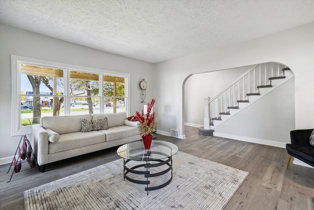 living room with arched walkways, stairway, baseboards, and wood finished floors