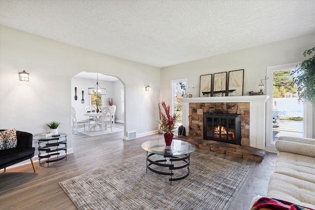 living area with visible vents, baseboards, a stone fireplace, wood finished floors, and arched walkways