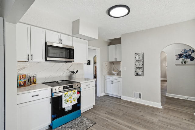kitchen with visible vents, light wood-style flooring, stainless steel appliances, arched walkways, and light countertops