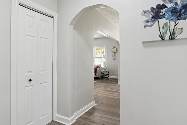 corridor with wood finished floors, arched walkways, and baseboards