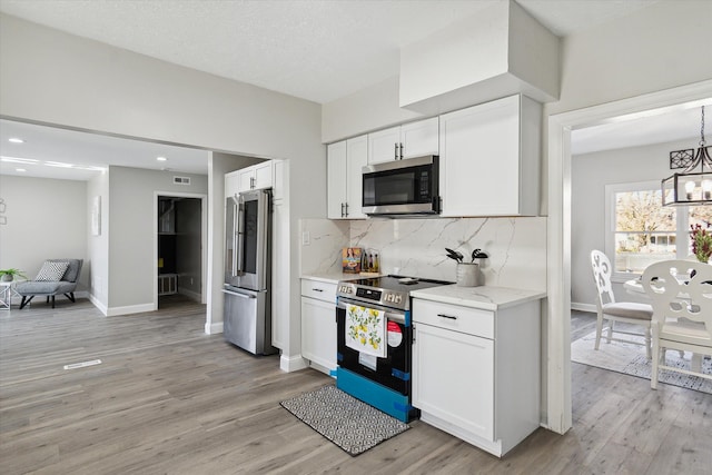 kitchen with light wood finished floors, decorative backsplash, stainless steel appliances, an inviting chandelier, and white cabinetry