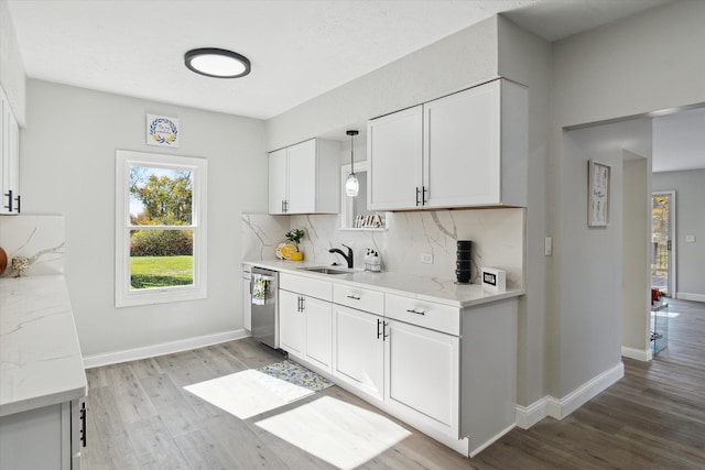 kitchen featuring tasteful backsplash, stainless steel dishwasher, light wood-style floors, white cabinets, and baseboards