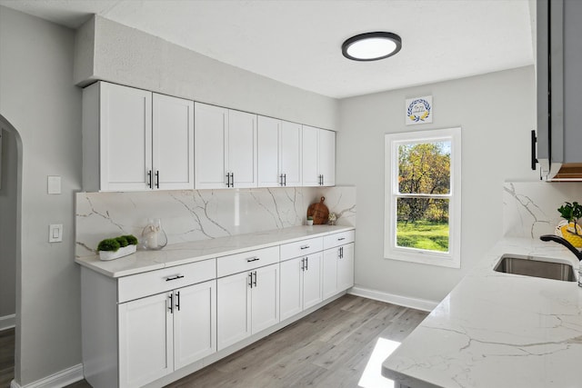 kitchen with light stone counters, decorative backsplash, light wood-style floors, and a sink