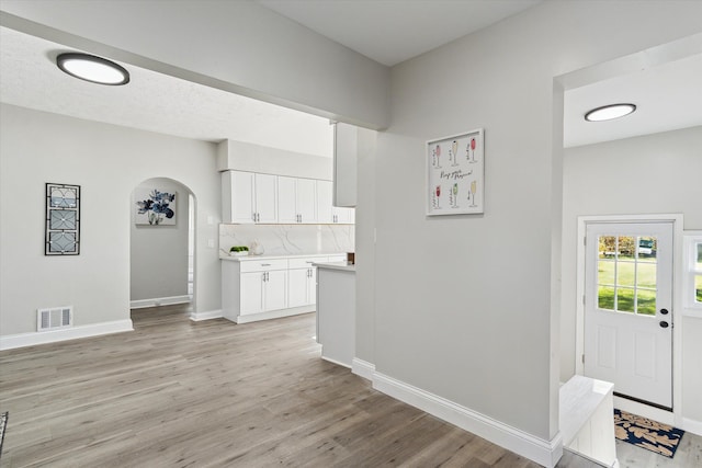 kitchen with arched walkways, decorative backsplash, light countertops, light wood-style floors, and white cabinetry