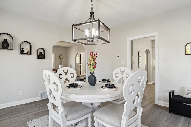 dining space featuring visible vents, wood finished floors, arched walkways, baseboards, and a chandelier