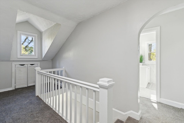 hallway featuring lofted ceiling, an upstairs landing, carpet floors, and a healthy amount of sunlight