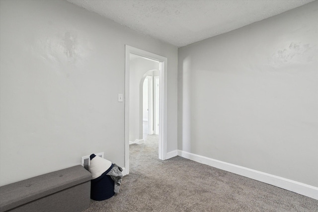 unfurnished room with arched walkways, a textured ceiling, baseboards, and carpet floors