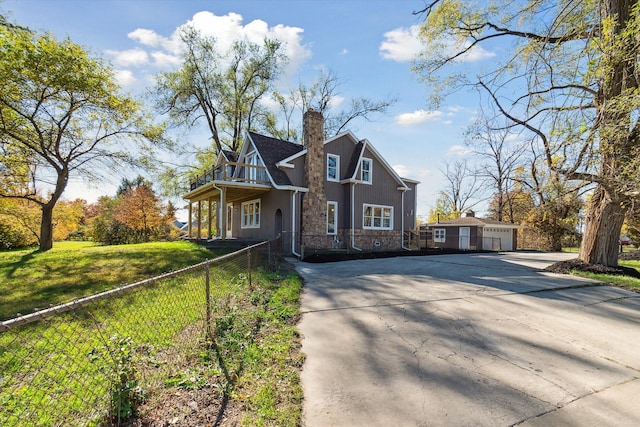 view of front of house with fence, concrete driveway, a front yard, an outdoor structure, and a chimney