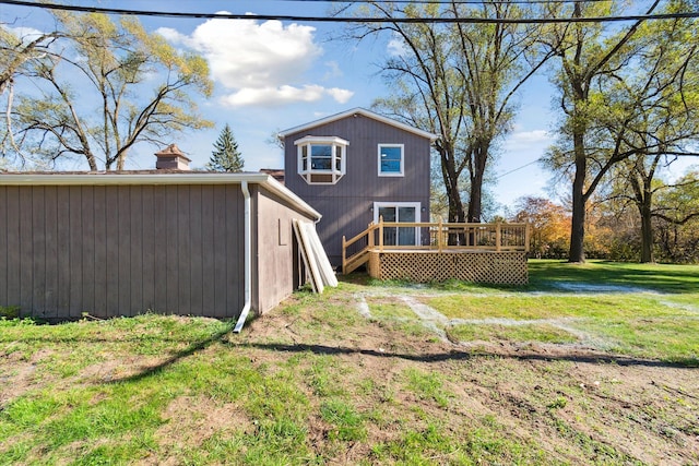 rear view of house featuring a chimney, a lawn, and a wooden deck