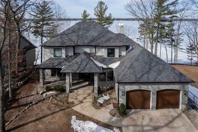 view of front of property with a shingled roof, a water view, concrete driveway, a chimney, and a garage