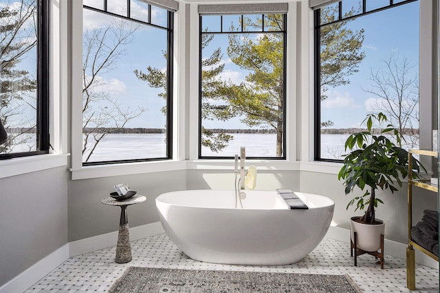 bathroom with tile patterned floors, a freestanding tub, baseboards, and a water view