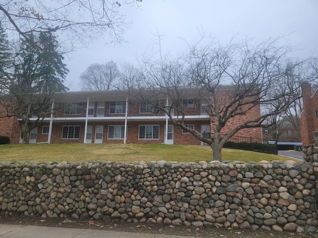 view of property with a front lawn, a balcony, and brick siding
