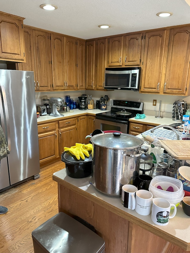 kitchen with light wood-style flooring, brown cabinets, stainless steel appliances, and light countertops