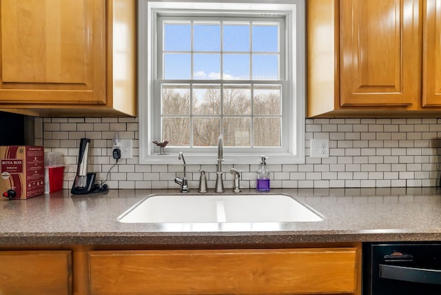 kitchen with brown cabinetry, a sink, decorative backsplash, and dishwasher