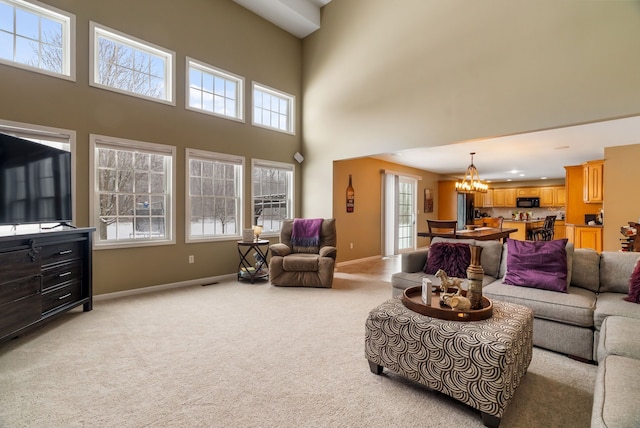 living area featuring baseboards, an inviting chandelier, light carpet, and a towering ceiling