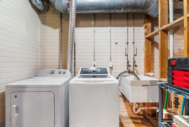 laundry area featuring laundry area, a sink, brick wall, and washer and dryer