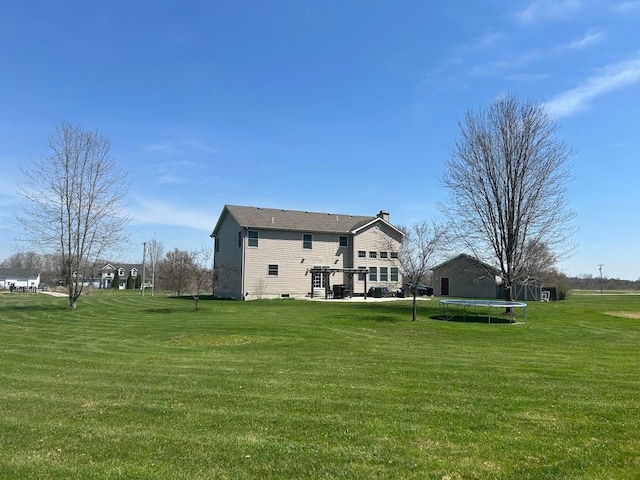rear view of house with a lawn and a trampoline