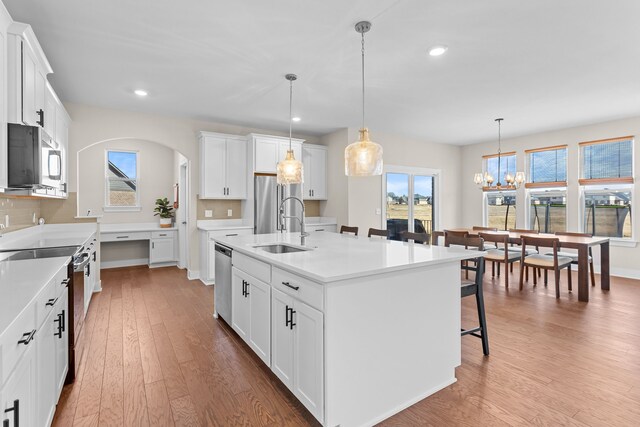 kitchen with a breakfast bar area, wood finished floors, arched walkways, stainless steel appliances, and backsplash