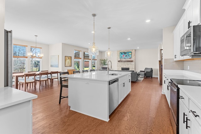 kitchen featuring light wood-style flooring, a sink, stainless steel appliances, a fireplace, and decorative backsplash