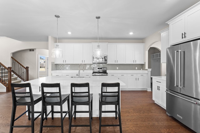 kitchen with a sink, light countertops, arched walkways, stainless steel appliances, and dark wood-style flooring