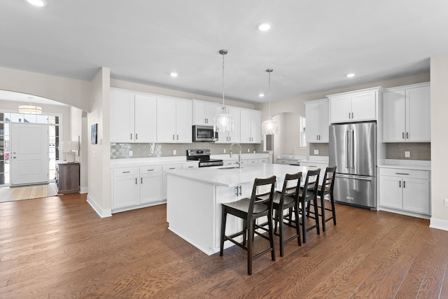 kitchen featuring a kitchen island with sink, dark wood-style flooring, arched walkways, light countertops, and appliances with stainless steel finishes