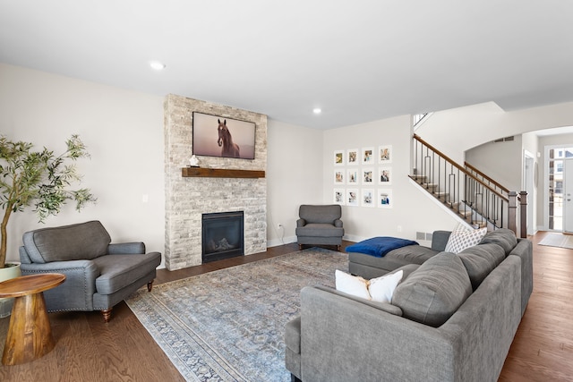 living area featuring wood finished floors, recessed lighting, arched walkways, stairs, and a stone fireplace