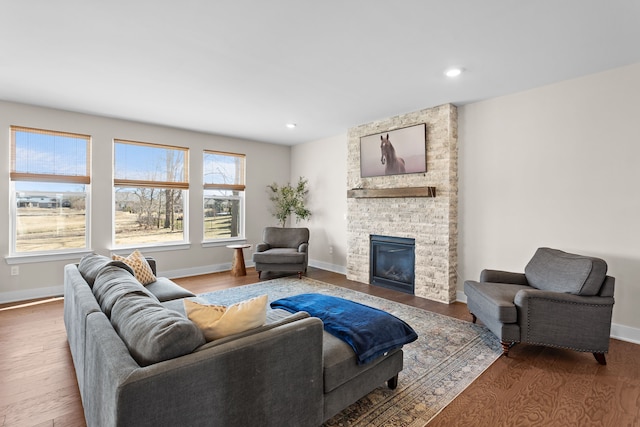 living area featuring a stone fireplace, recessed lighting, baseboards, and wood finished floors