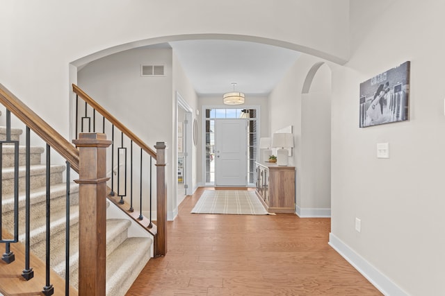 foyer entrance with visible vents, baseboards, stairs, light wood-style flooring, and arched walkways