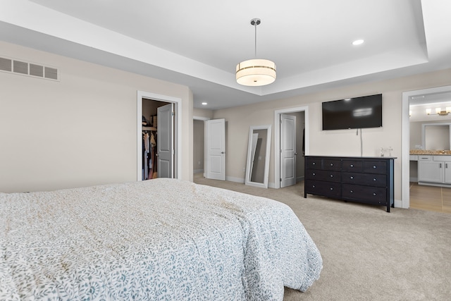 bedroom with light carpet, visible vents, a walk in closet, and a raised ceiling
