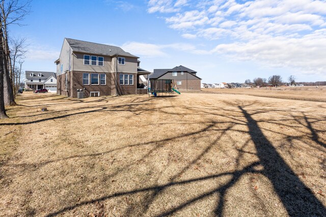 back of house featuring brick siding, a playground, and central AC