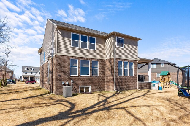 rear view of house with brick siding, central air condition unit, a playground, and a yard