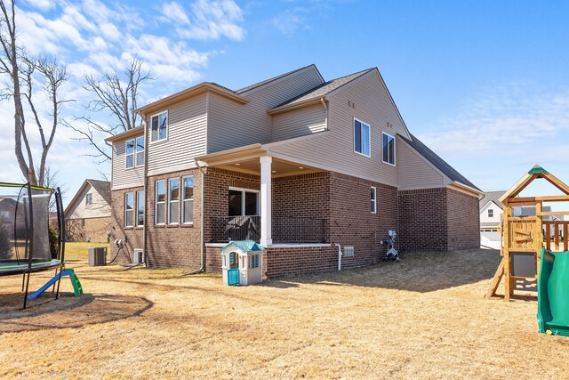 back of property with brick siding, central air condition unit, a playground, and a trampoline