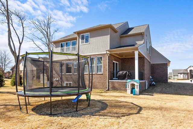 rear view of property with a trampoline and brick siding