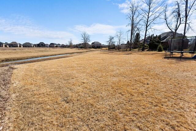 view of yard with a residential view, a trampoline, and a water view