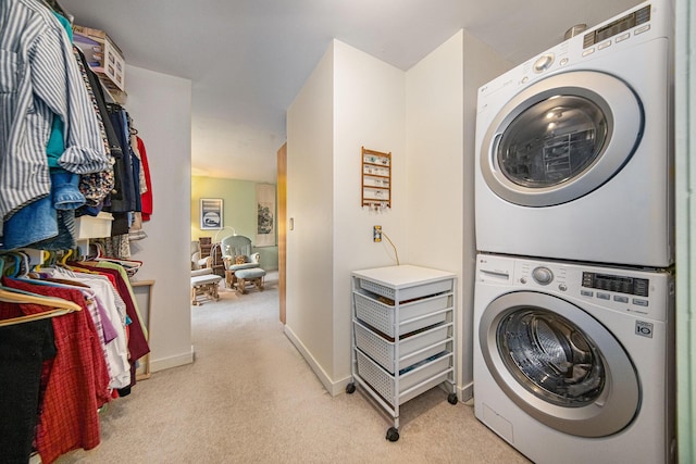 clothes washing area featuring laundry area, light colored carpet, stacked washing maching and dryer, and baseboards